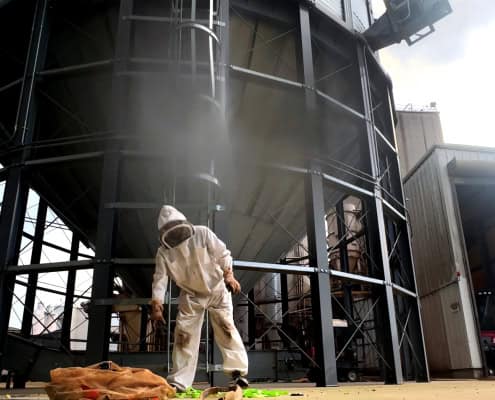 Industrial beekeeping facility with person in protective suit, beekeeping equipment, and large metal storage tanks.