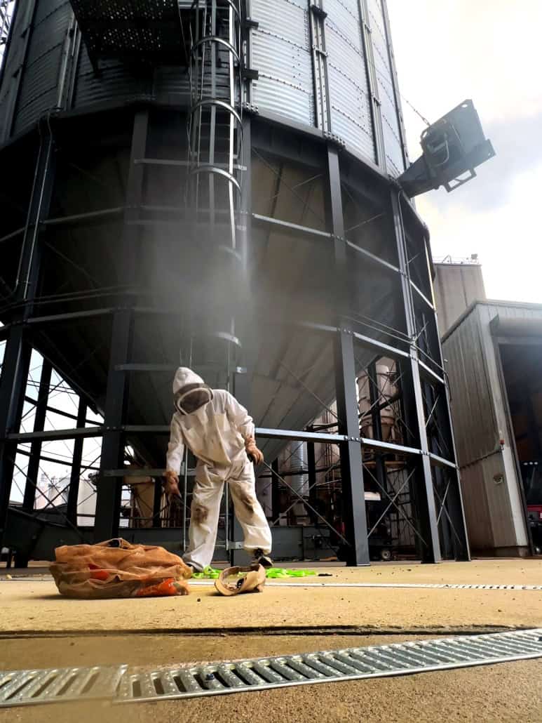 Industrial beekeeping facility with person in protective suit, beekeeping equipment, and large metal storage tanks.