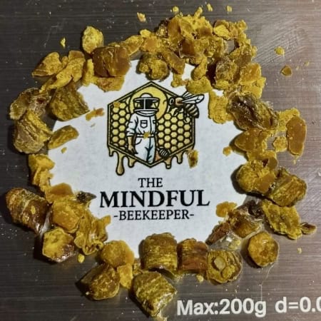 Golden bee pollen granules on The Mindful Beekeeper logo, highlighting natural honeybee products.