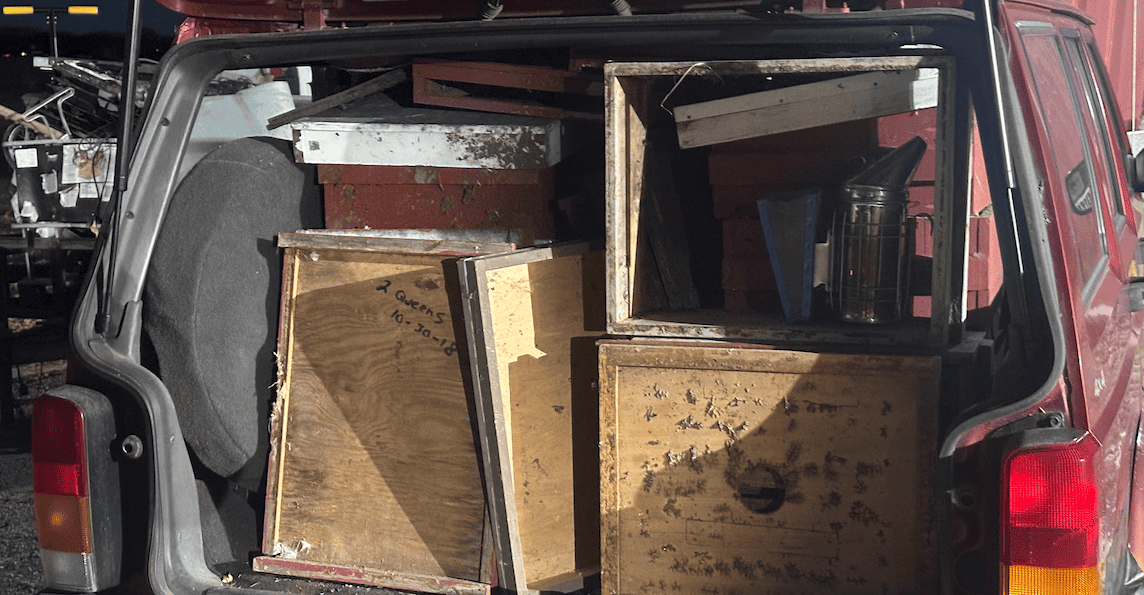 2. cluttered bee equipment and wooden hive boxes in the back of a red vehicle, ready for beekeeping.