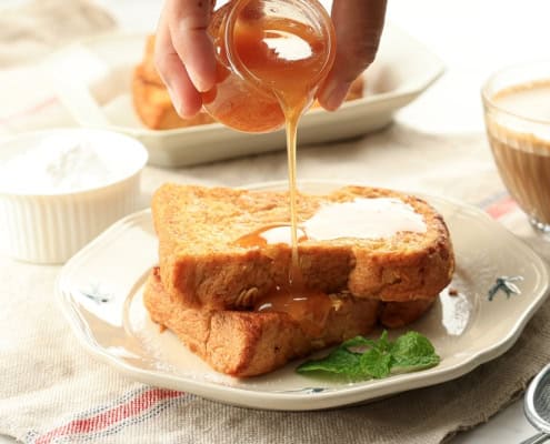 Sweet honey being drizzled over French toast with syrup and fresh mint, served with coffee and cream.